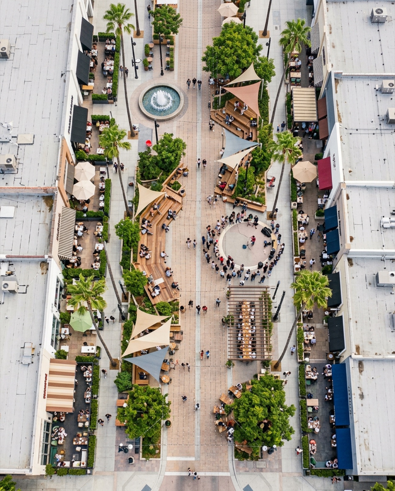 Aerial of the promenade by day - fountain, shade sails, dining terraces and a gathered crowd